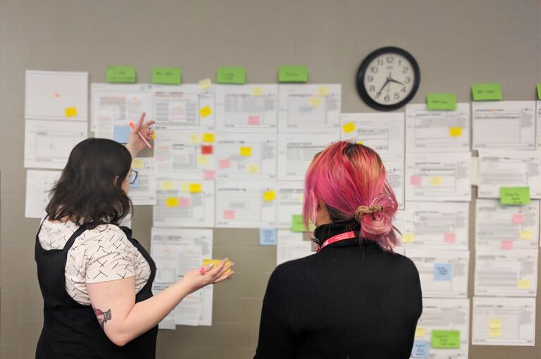 From left: Code for Canada fellows Siobhan Ozege and Joey Hua review user research data contained on numerous printouts and sticky notes.