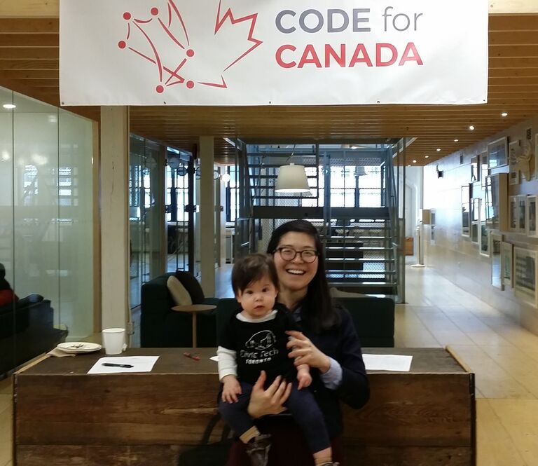 Dorothy at Code for Canada's launch, holding her child in front of a "Code for Canada" banner
